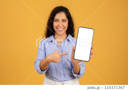 Confident young woman with curly hair presents a smartphone with a blank screen 110371367