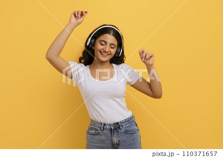 Joyful young pretty indian woman with headphones dancing 110371657