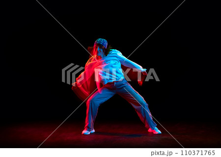 Young woman in casual clothes dancing hip hop isolated over black background in neon light with mixed lights effect Young woman in casual clothes dancing hip hop isolated over black background in neon light with mixed lights effect 110371765