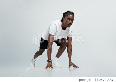 Focused black man in athletic wear poised in starting position for sprint 110371773