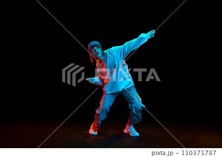 Artistic young woman in sportive casual clothe dancing hip hop isolated over black background in neon light 110371787