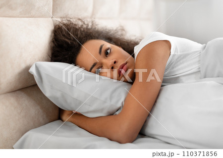 Unhappy black young woman lying alone awake in domestic bedroom 110371856