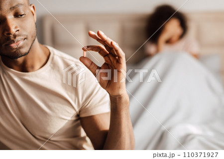 black man taking potency pill sitting in bed with girlfriend 110371927