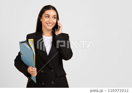 Businesswoman on phone with documents in hand, smiling Businesswoman on phone with documents in hand, smiling 110372012