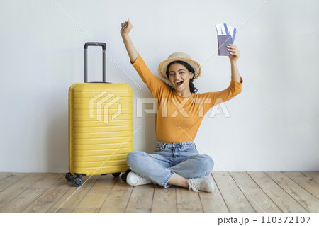 Joyful indian woman sitting on floor with her passport and boarding passes Joyful indian woman sitting on floor with her passport and boarding passes 110372107