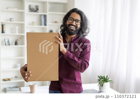 Happy Young Indian Man Embracing Cardboard Box With Delivery At Home Happy Young Indian Man Embracing Cardboard Box With Delivery At Home 110372121