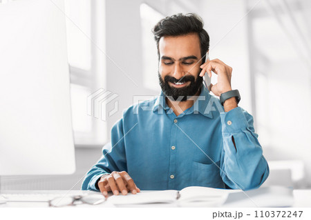 Joyful indian man conversing on phone with planner and glasses 110372247