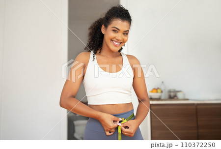 Athletic young woman measuring waist smiling to camera at home 110372250