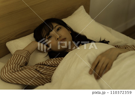 ベッドの布団に入る若い女性 110372359
