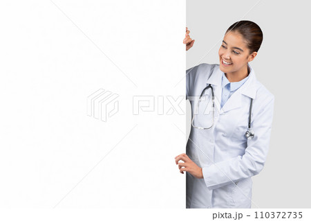 Enthusiastic Caucasian millennial doctor peering around a blank whiteboard 110372735
