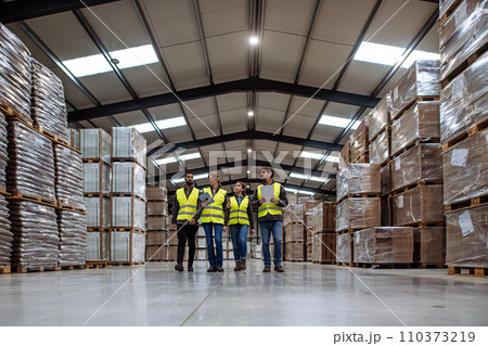 Front view of warehouse workers walking in warehouse. Team of warehouse workers preparing products for shipment. 110373219
