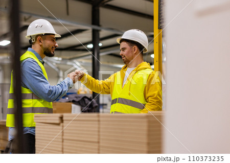 Young man with Down syndrome working in modern factory, fist bump with colleague, teamwork. Concept of workers with disabilities, support in workplace. Young man with Down syndrome working in modern factory, fist bump with colleague, teamwork. Concept of workers with disabilities, support in workplace. 110373235
