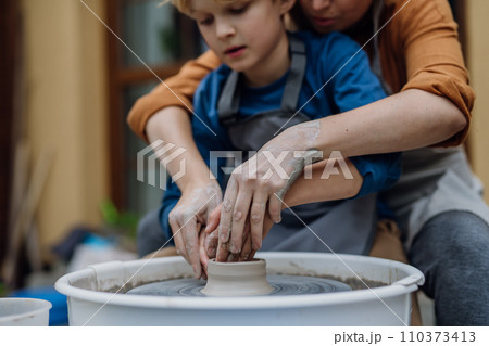 Mother teaching son how make pottery on pottery wheel. Child creative activities and art. Boy making pottery, having fun. Happy family moment. 110373413