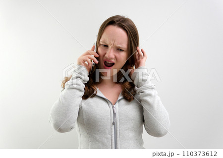 Frustrated annoyed sad woman with mobile phone standing intside white background 110373612