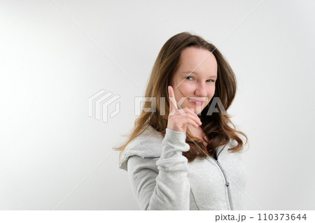 a young teenage girl raised her index finger up, squinting her eyes, there is an idea, a trick, happy, on a white background, space for advertising text 110373644