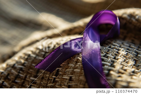 A close-up of a purple ribbon, the symbol of overdose awareness, pinned to a fabric with subtle textures 110374470