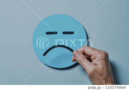 man attaching a sad mouth to a blue paper face 110374944