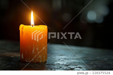 A single candle burning brightly in a dark room, casting a gentle glow. The candle symbolizes remembrance and awareness 110375528