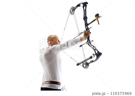 Bald man in his 40s, archery athlete exercising with the bow, aiming upwards isolated over white studio background. Archery sport, competition Bald man in his 40s, archery athlete exercising with the bow, aiming upwards isolated over white studio background. Archery sport, competition 110375969