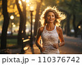 Mature blond woman jogging in the park at sunset 110376742