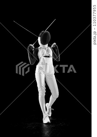 Full length portrait of professional sportswomen, master of blade, skillfully intertwined her swords behind her back in striking pose against black background. 110377955