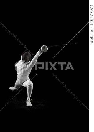 Female fencer glides across floor, her blade in motion against black studio background. Sportsman focused and determined. Female fencer glides across floor, her blade in motion against black studio background. Sportsman focused and determined. 110377974