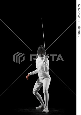 Swordswoman, professional female fencer's poised stance, against black studio background. Intensity and excitement of fencing. Swordswoman, professional female fencer's poised stance, against black studio background. Intensity and excitement of fencing. 110377979