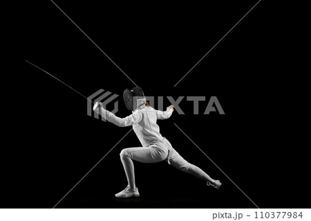 Fencer's footwork and poised stance in mid-bout against pristine black studio background. Tactical aspect dynamic sport. 110377984
