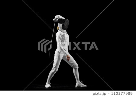 Fencer's flawless attack, precision evident in her form against black studio background, epitomizing pursuit of perfection. Concept of active lifestyle. 110377989