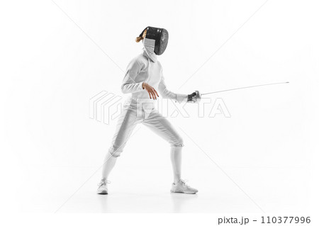 Female athlete in fencing gear showcasing her impeccable form, sword poised for action against white studio background. Confidence and strength. 110377996