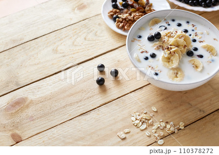 Oatmeal porridgewith bananas, nuts, raisins, blueberries and milk on table on wooden  background.  Healthy breakfast and diet food. Top view 110378272