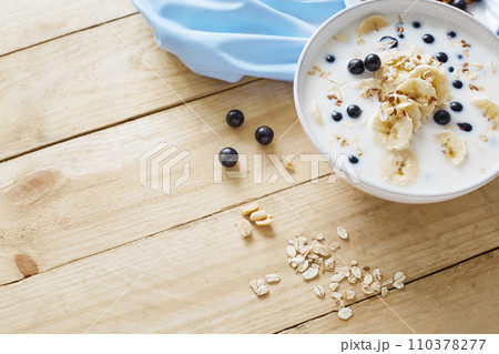 Oatmeal porridgewith bananas, nuts, raisins, blueberries and milk on table on wooden  background.  Healthy breakfast and diet food. Top view 110378277