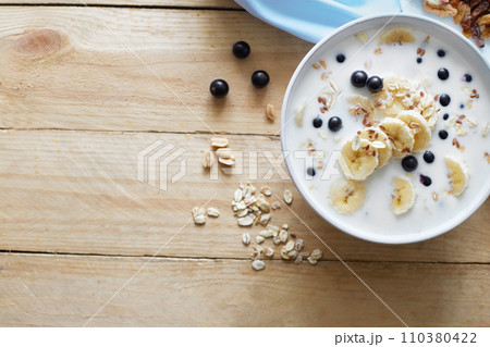 Oatmeal porridgewith bananas, nuts, raisins, blueberries and milk on table on wooden  background.  Healthy breakfast and diet food. Top view 110380422