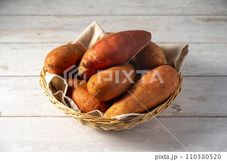 Whole raw sweet potatoes in a basket, on bright background. 110380520