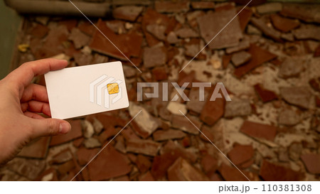Woman's hand with a bank card against the background of pieces of broken tiles on the floor. The concept of starting repairs and the high cost of repairs. Woman's hand with a bank card against the background of pieces of broken tiles on the floor. The concept of starting repairs and the high cost of repairs. 110381308