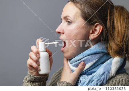 A woman with a sore throat sprays medicine aerosol spray down her throat A woman with a sore throat sprays medicine aerosol spray down her throat 110383028