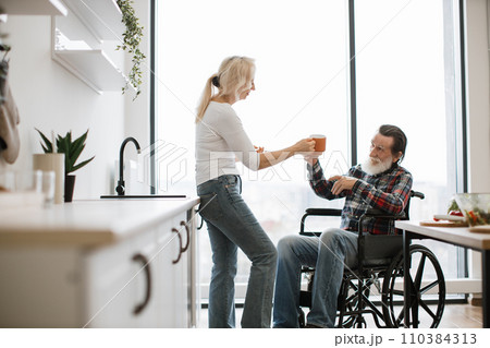 Pensioners wife and husband in wheelchair drinking hot drinks from mugs Pensioners wife and husband in wheelchair drinking hot drinks from mugs 110384313