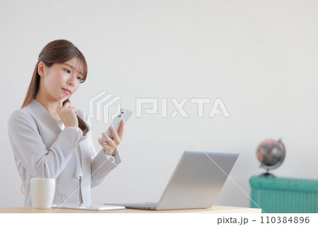 あごに指を当てスマホを見て考えるビジネスウーマン1 110384896