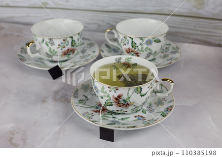 Brewing green tea in a bag in a cup on a saucer from a tea set with a pattern of flowers 110385198