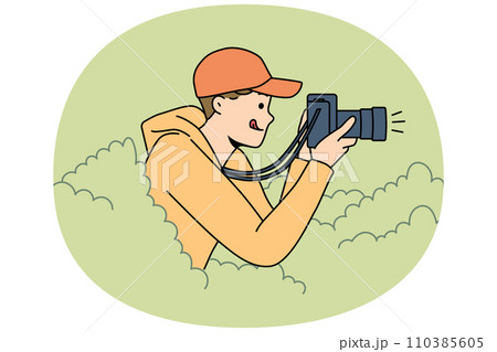 Young man reporter hide in bushes make pictures 110385605