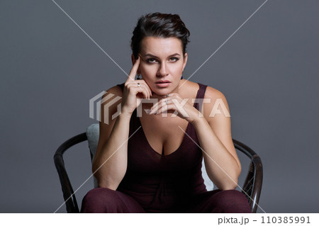 Fashionable young woman posing sitting in chair on dark gray studio background 110385991