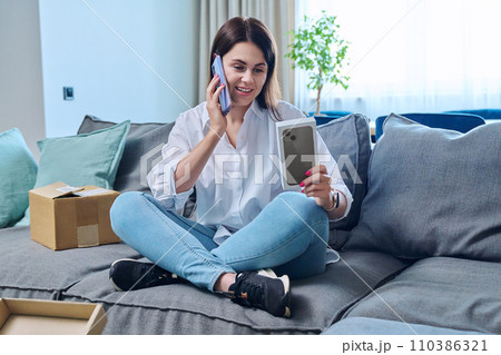 Young woman sitting at home unpacking cardboard box with online shopping 110386321