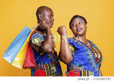 African american man carrying bags with purchase while shopping in mall with woman. Black couple in relationship enjoying sale in store, buying clothes and holding paperbags 110386795
