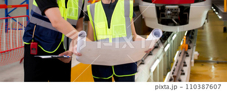 Young caucasian engineer man and woman or worker looking blueprint and checking electric train. Young caucasian engineer man and woman or worker looking blueprint and checking electric train. 110387607