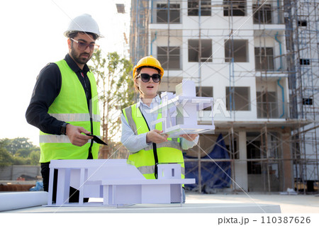 Team architect and builder talking and holding model house at construction site. Team architect and builder talking and holding model house at construction site. 110387626