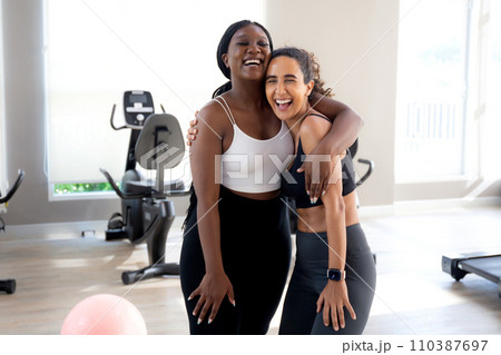 Two young woman talking and hug with fun in the gym, woman in sportswear and friend or coach relax. 110387697