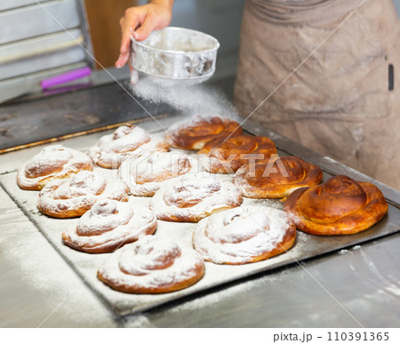 Baker hands dusting baked ensaimadas with powdered sugar Baker hands dusting baked ensaimadas with powdered sugar 110391365