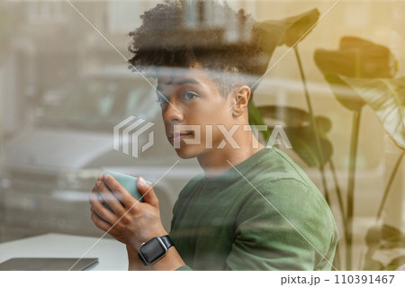 Shot from outside african american guy drinking coffee at cafe 110391467