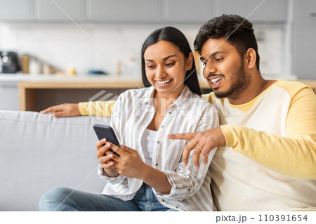 Happy Young Indian Couple Using Mobile Phone Together At Home Happy Young Indian Couple Using Mobile Phone Together At Home 110391654