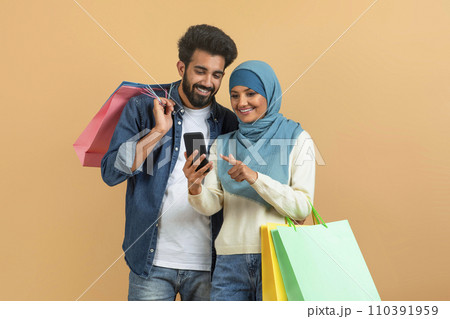Shopping App. Happy Muslim Spouses Holding Shopper Bags And Using Smartphone Shopping App. Happy Muslim Spouses Holding Shopper Bags And Using Smartphone 110391959